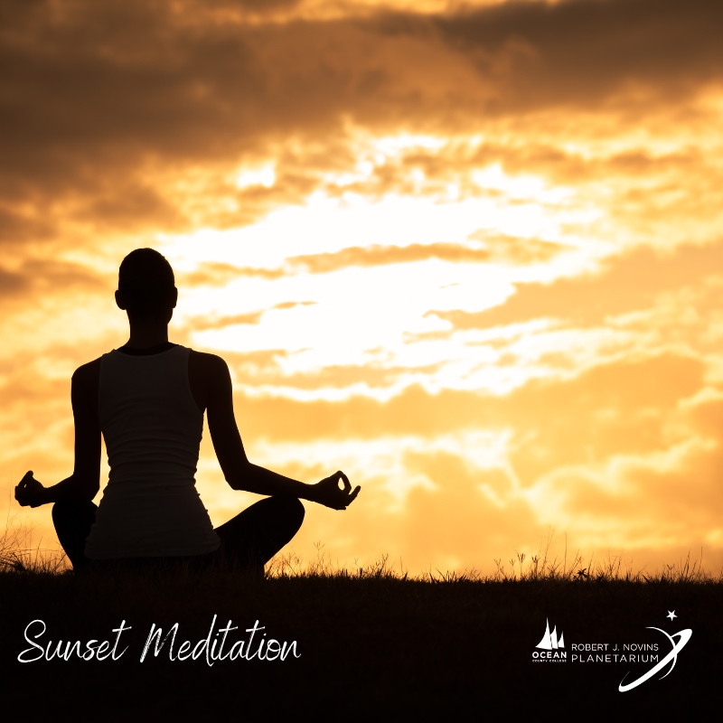 A silhouette of a person meditating on grass at sunset with a bright orange sky.